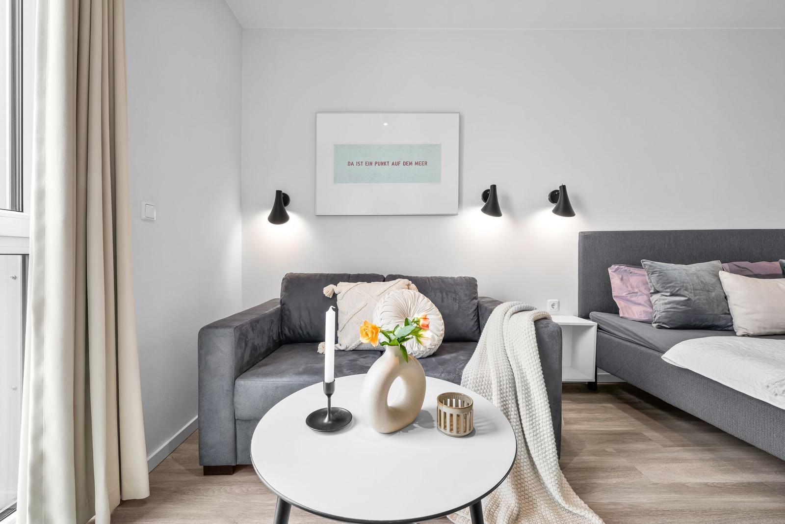 Ein Wohnbereich mit grauem Sofa, runden Tisch und Wandbild.