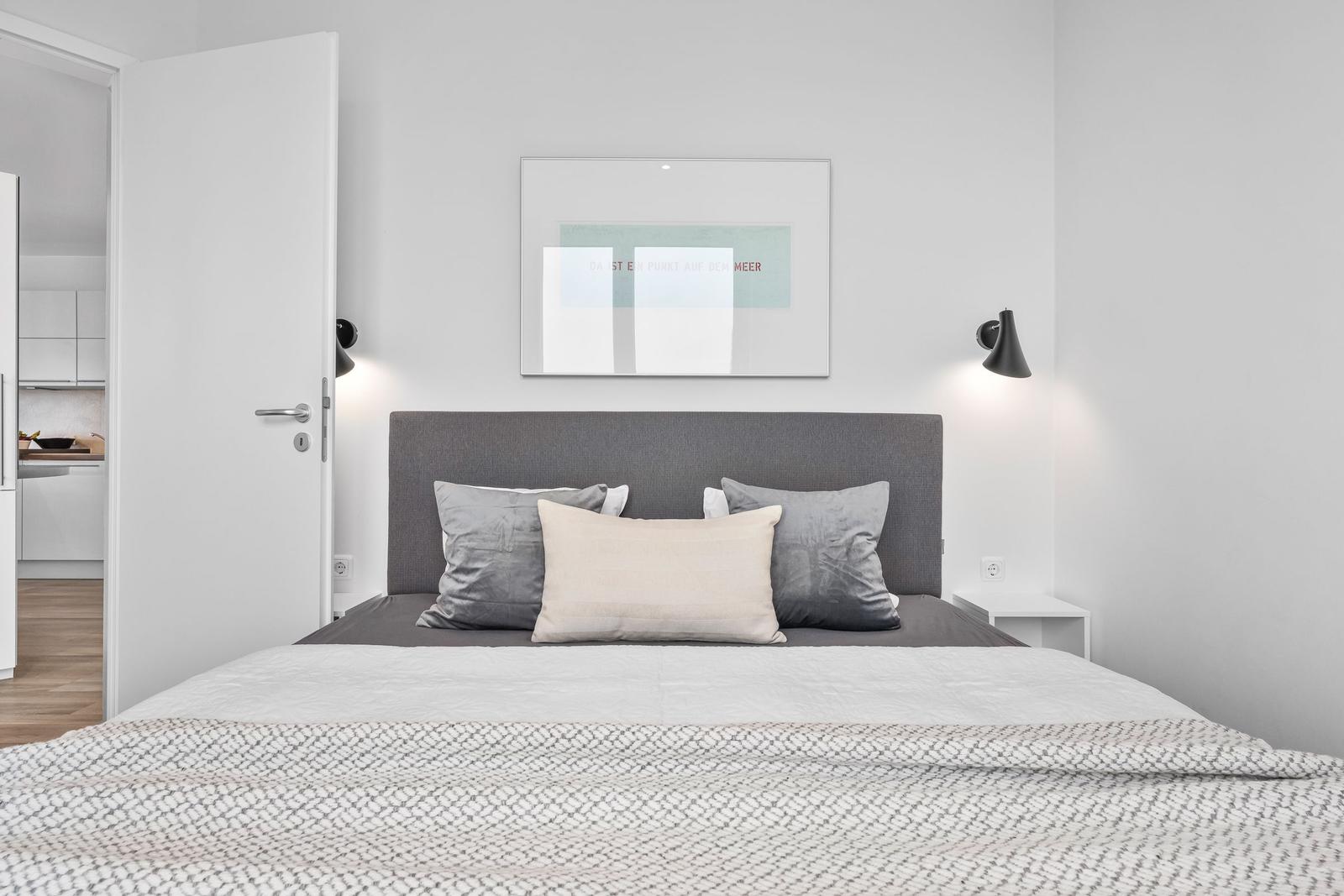 Schlafzimmer mit Bett, Wandbild und Nachttischen. Tür führt in die Küche.