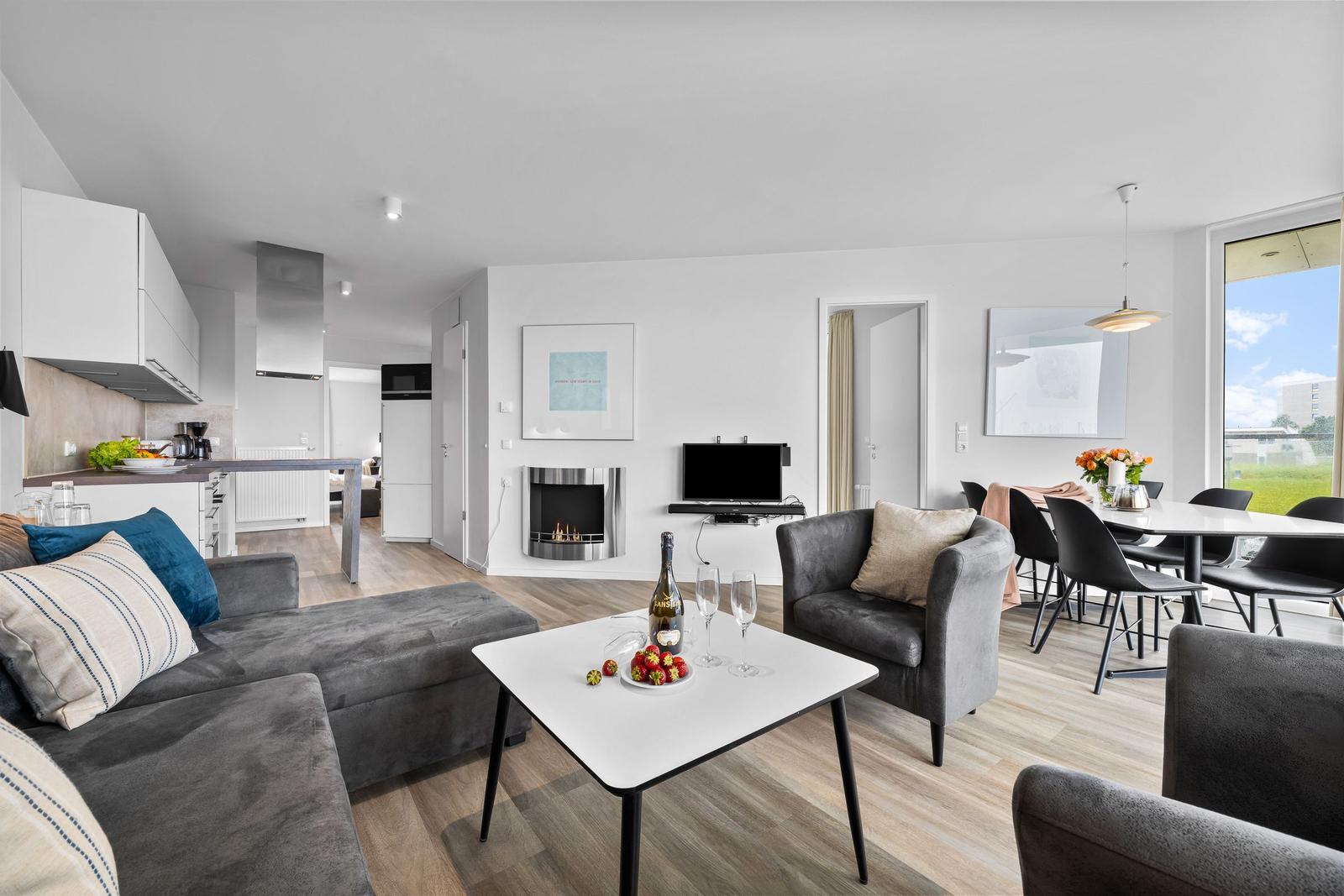Wohnzimmer mit Sofa, Esstisch und Kamin. Küche und Schlafzimmer sind sichtbar.