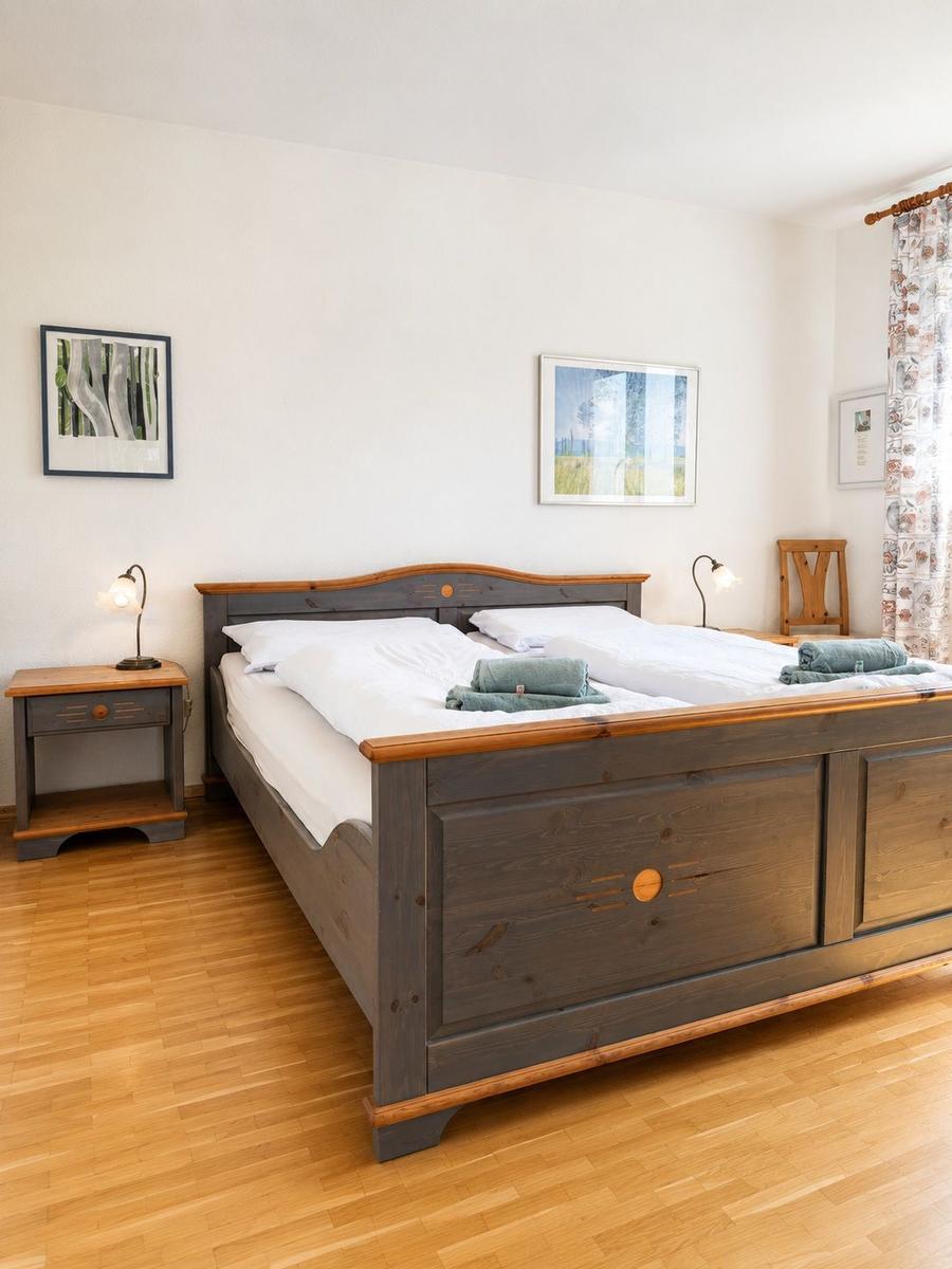 Schlafzimmer mit Holzbett, Nachttisch und Bildern an der Wand.