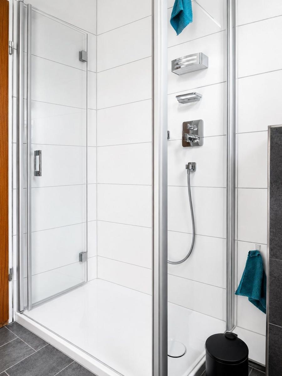 Duschkabine mit Glaswand, Duschbrause und Handbrause an der Wand.