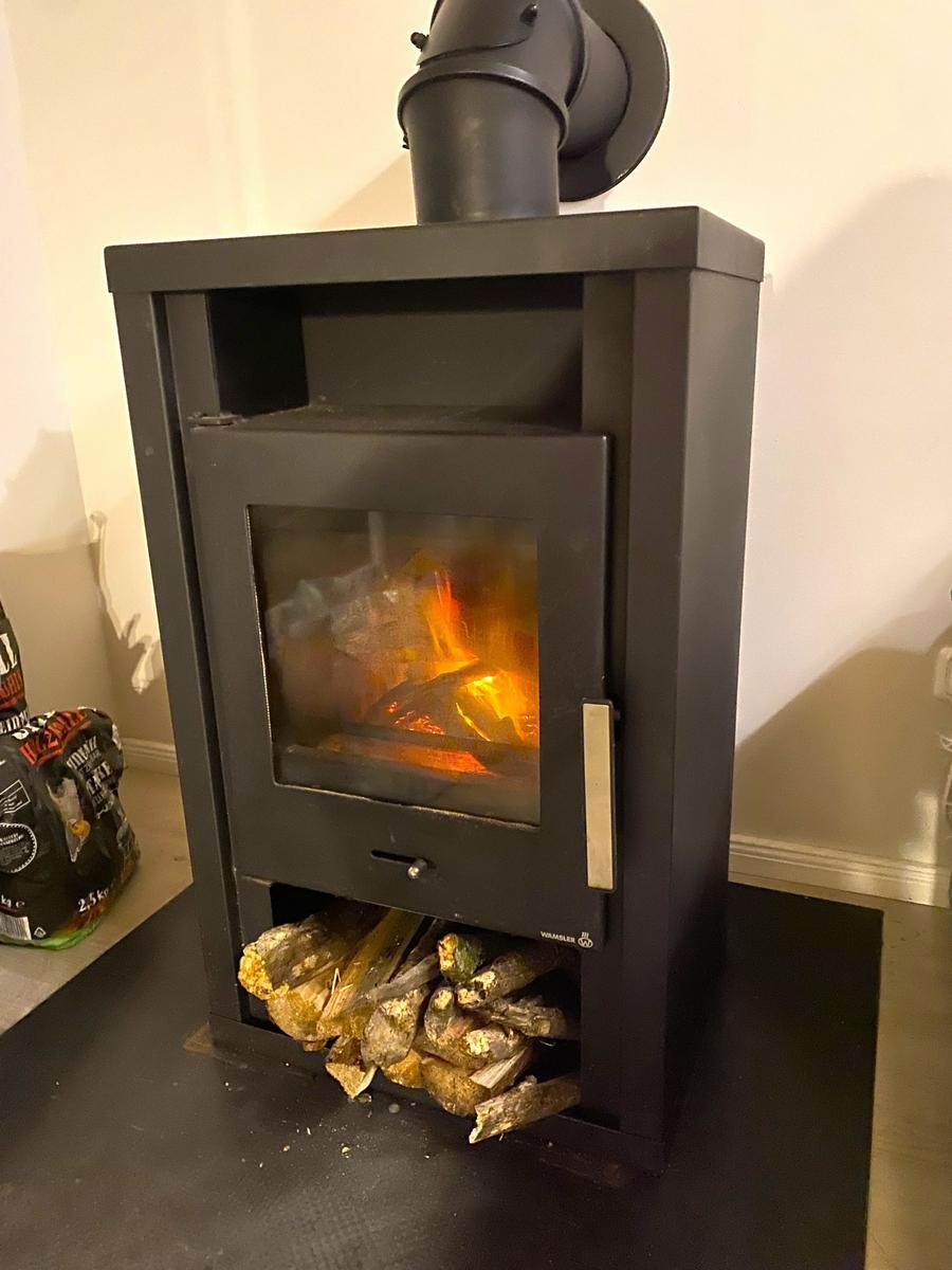 Holzofen mit brennendem Feuer und Holzstapel darunter.
