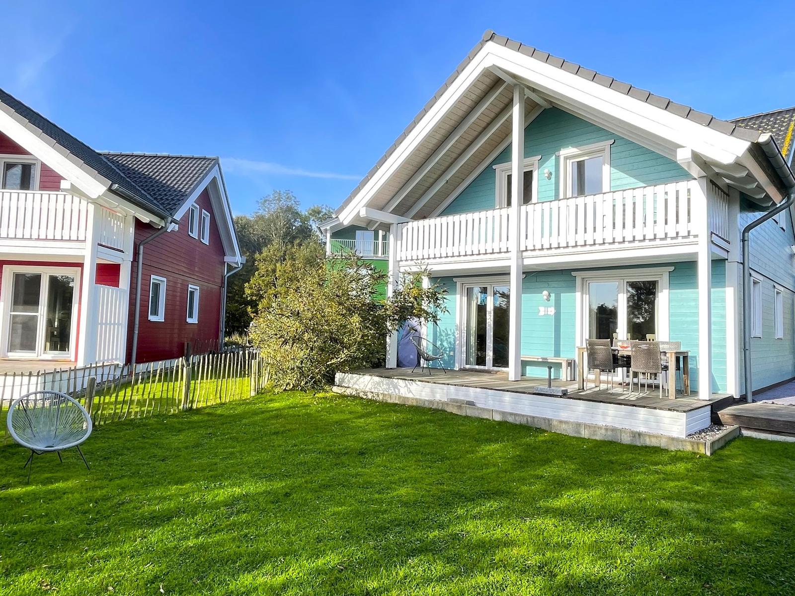 Ein hellblauer Ferienhaus mit Terrasse und Garten. Neben einem roten Haus.