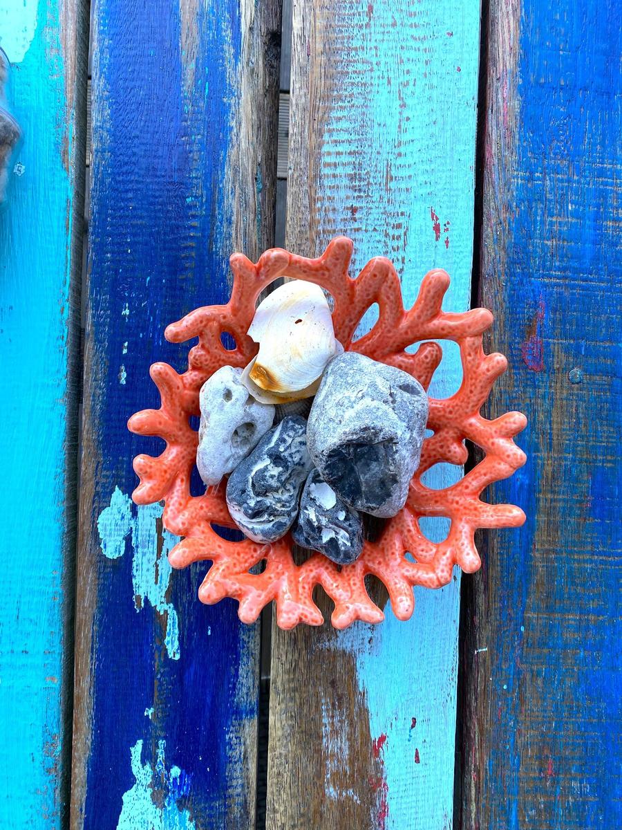 Ein roter Korallenkorb mit Steinen und Muscheln auf blauem Holz