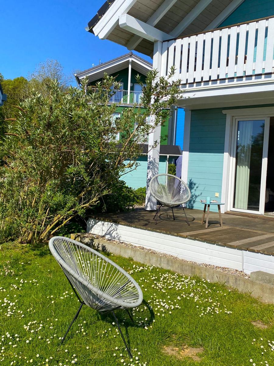 Terrasse mit Sitzgelegenheit und Garten mit Stuhl. Hintergrund: Holzhaus mit Balkon.