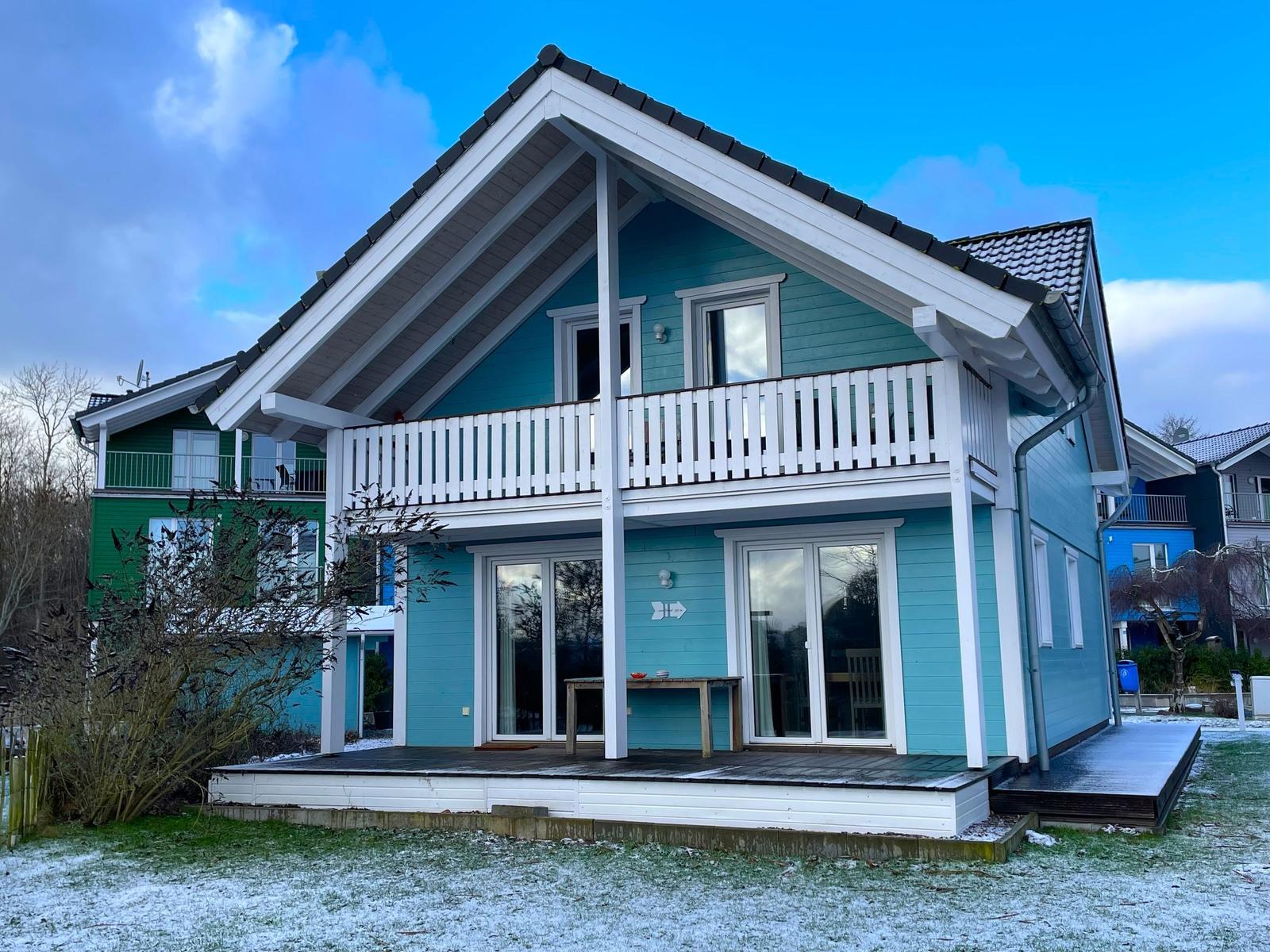 Ein zweistöckiges Haus mit Balkon und Terrasse. Der Boden ist schneebedeckt.