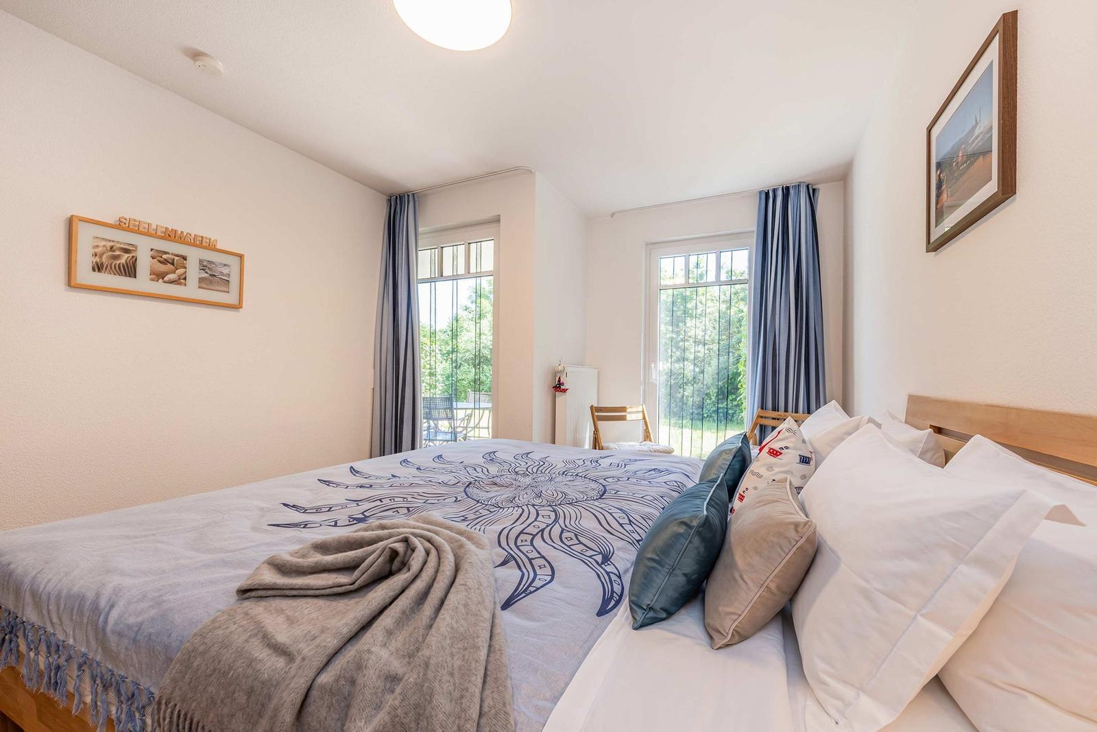 Schlafzimmer mit Doppelbett, Fenstern und Wandbildern.