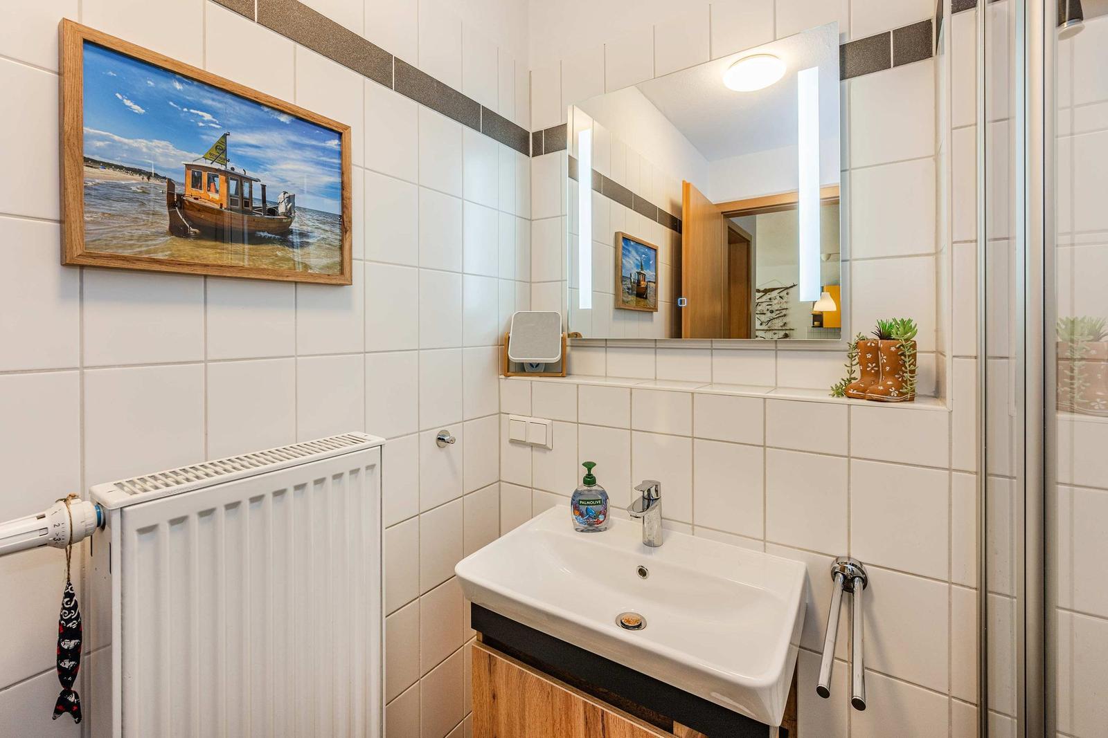 Badezimmer mit Waschbecken, Spiegel, Heizung und Wandbild.