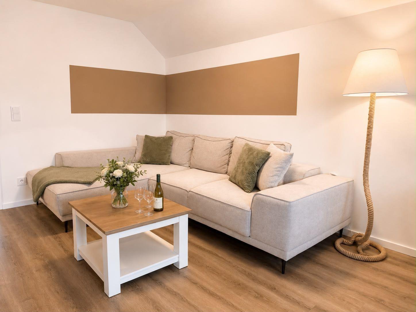 Wohnzimmer mit Ecksofa, Tisch und Stehlampe.