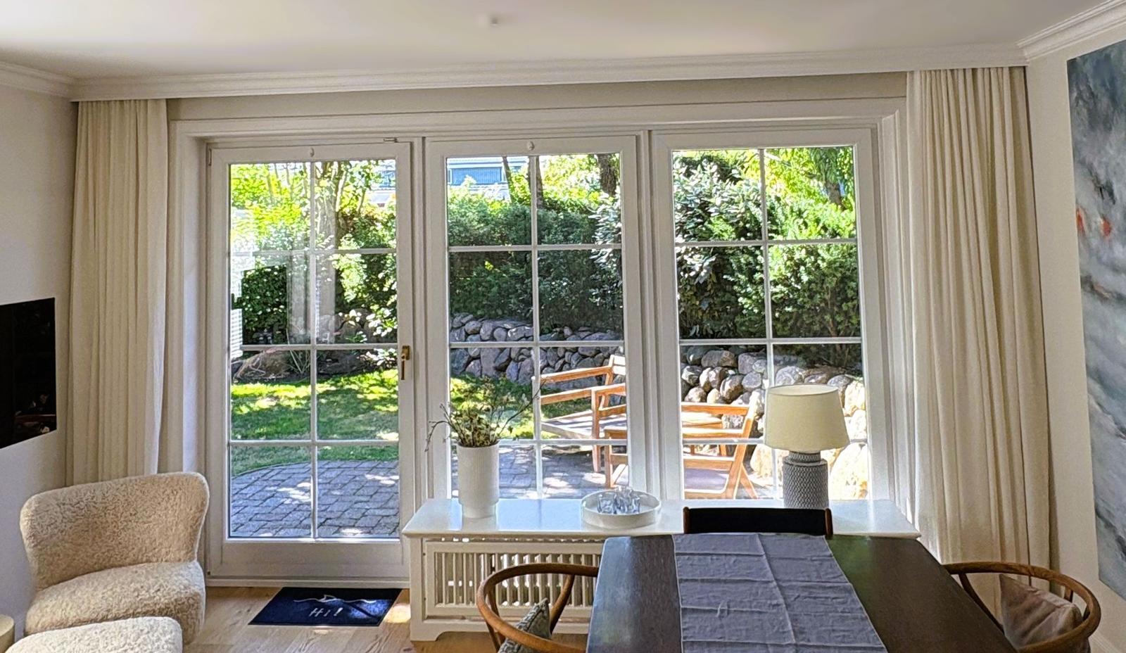 Durchgehende Glastüren führen auf eine Terrasse mit Garten. Essbereich und Sitzgelegenheit im Raum.