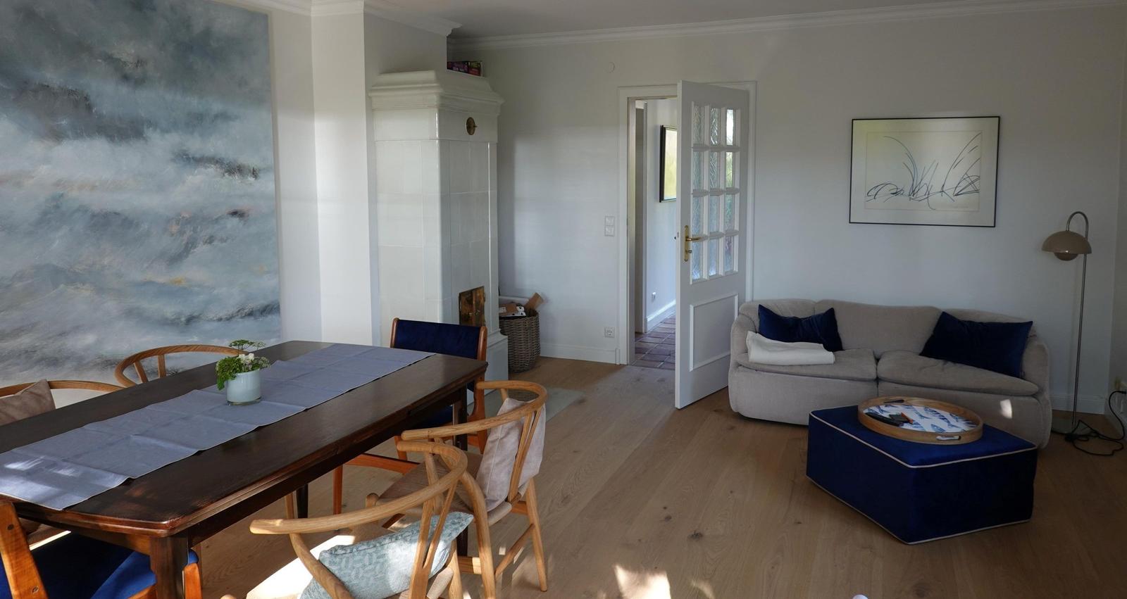 Essbereich mit Tisch und Stühlen, Wohnbereich mit Sofa und Kissen, Holzboden und Wandbild.