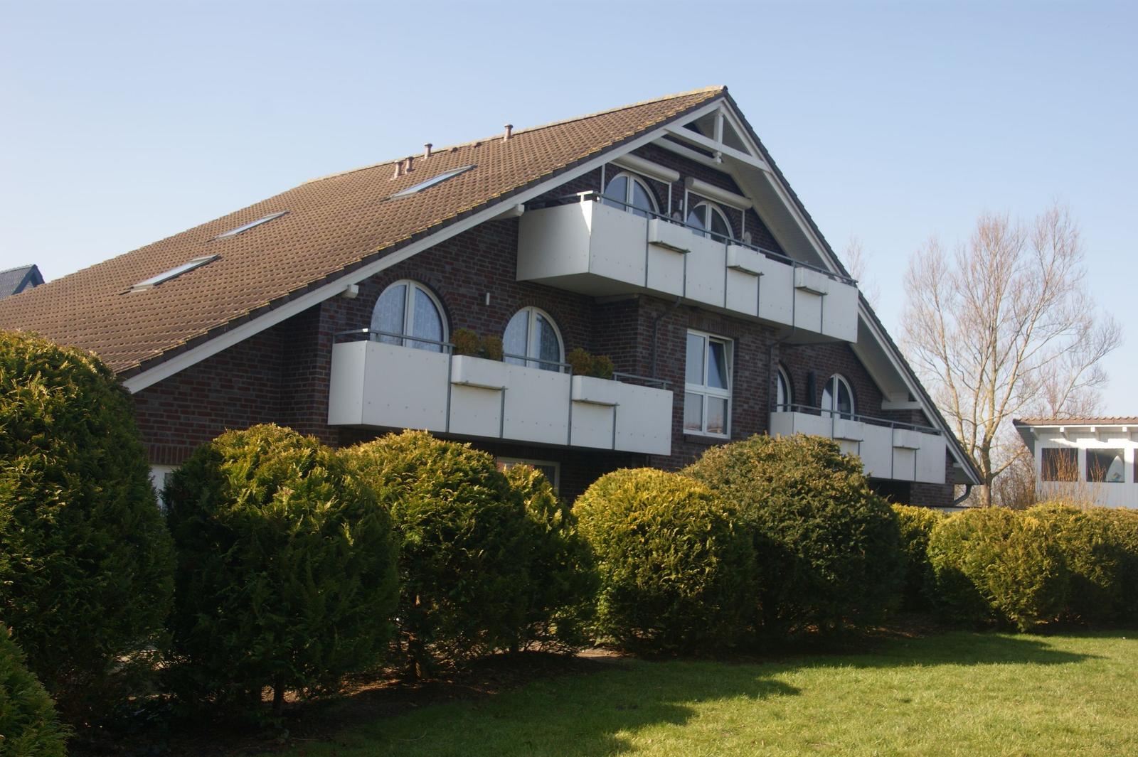 Zweistöckiges Haus mit Balkonen und Dachfenstern, umgeben von grünen Hecken.