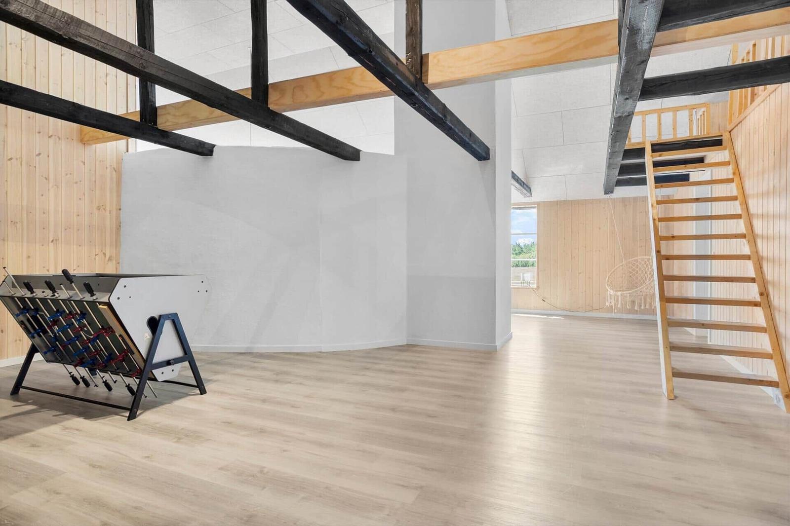 Großes Zimmer mit Holzboden, Treppe und Tischfußball. Holzbalken und Fenster sichtbar.