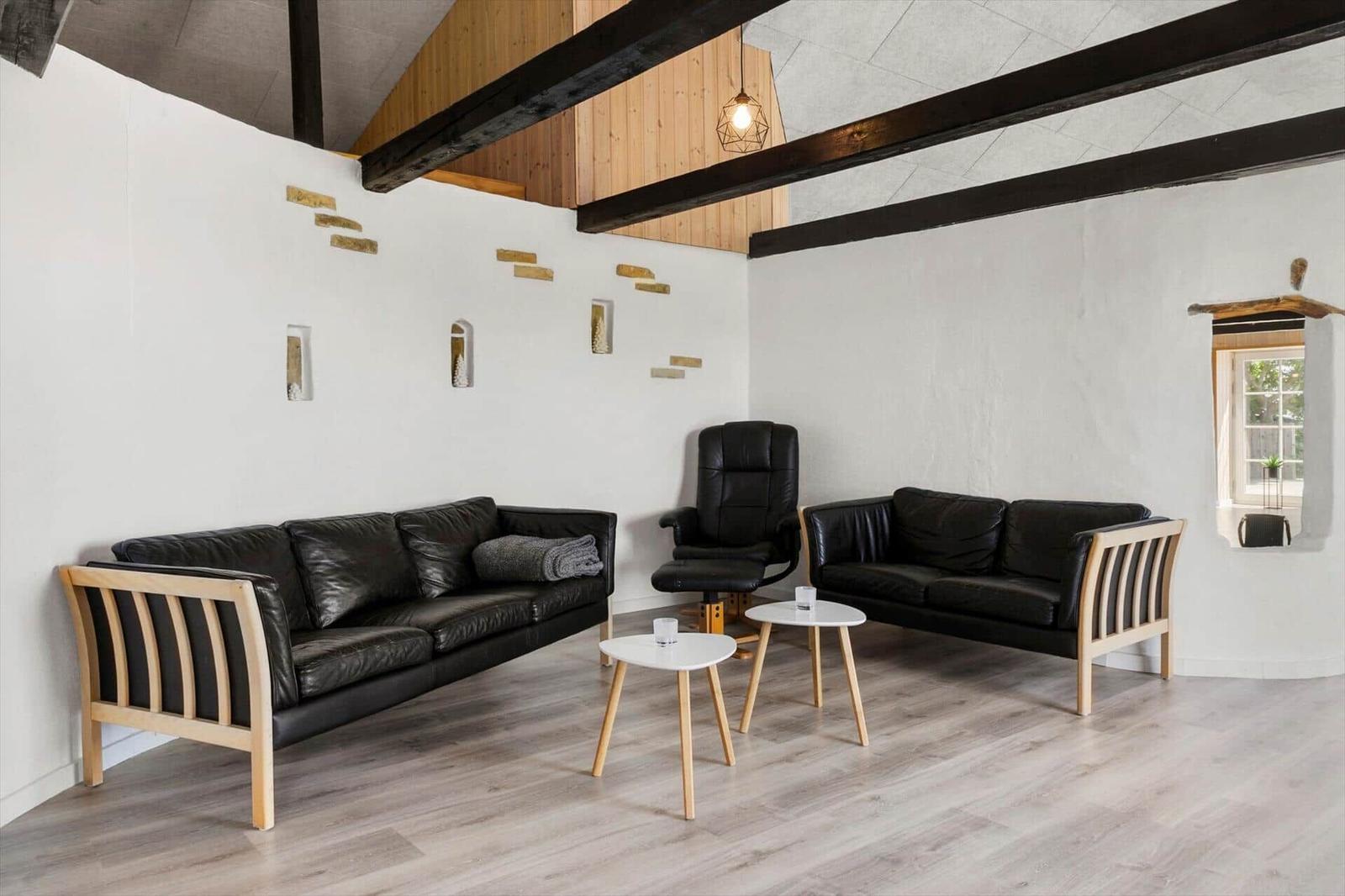 Zwei schwarze Sofas, ein Sessel und zwei Tische in einem Raum mit Holzbalken und Fenster.