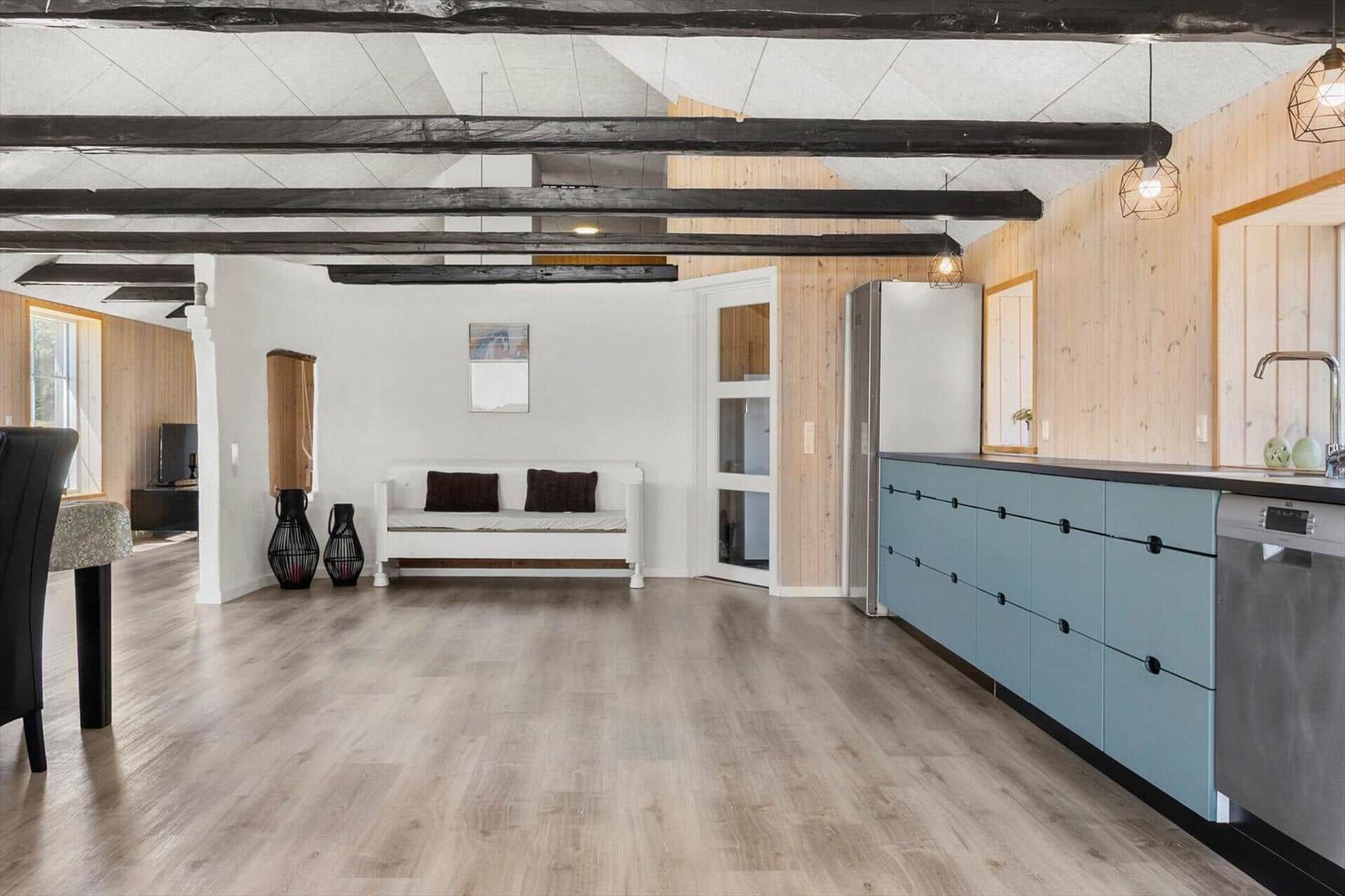 Wohn- und Küchenbereich mit Holzboden, Balken und blauen Schränken.