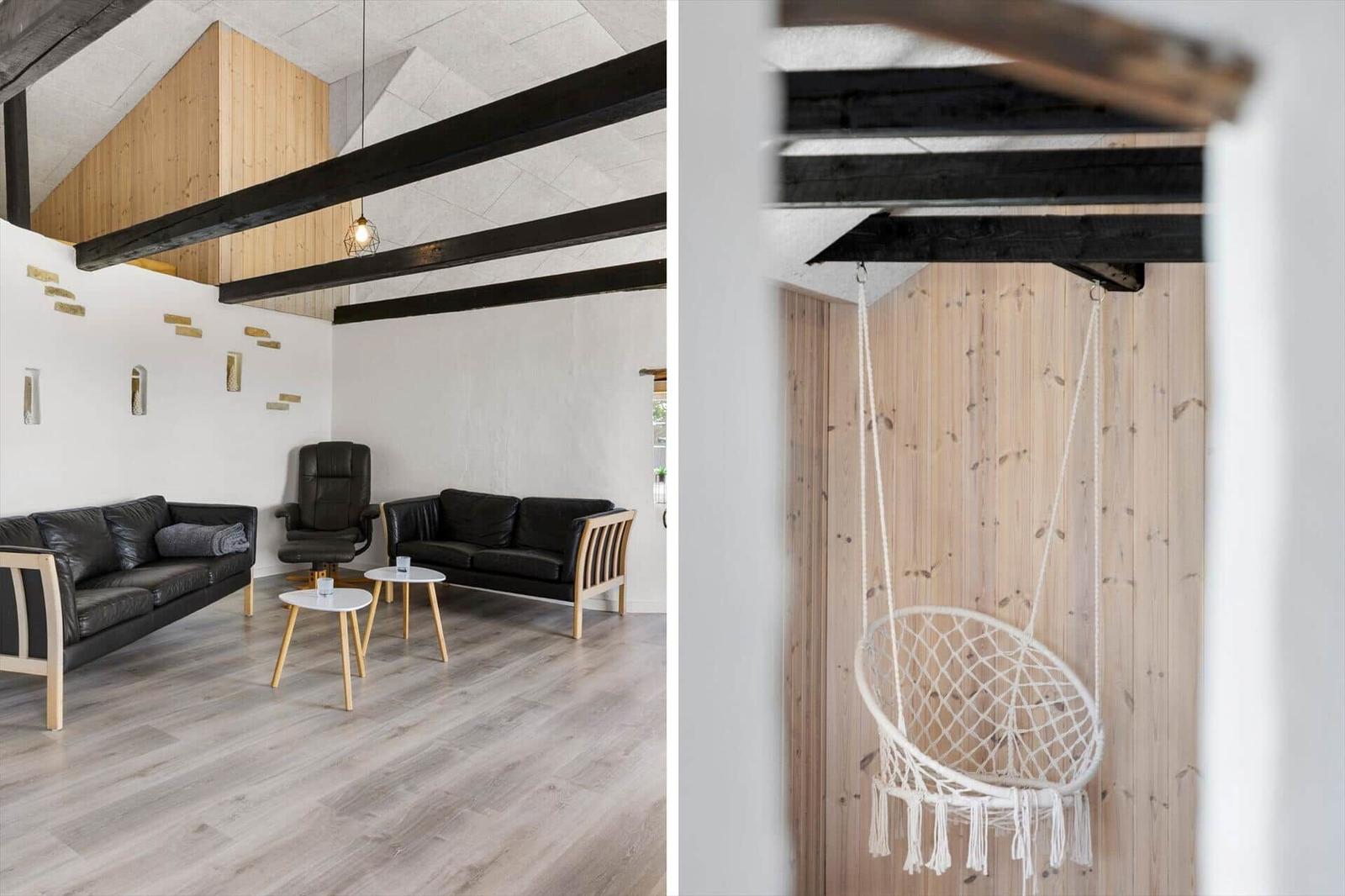 Wohnbereich mit schwarzen Sofas und Holzbalken. Hängesessel aus weißem Garn.