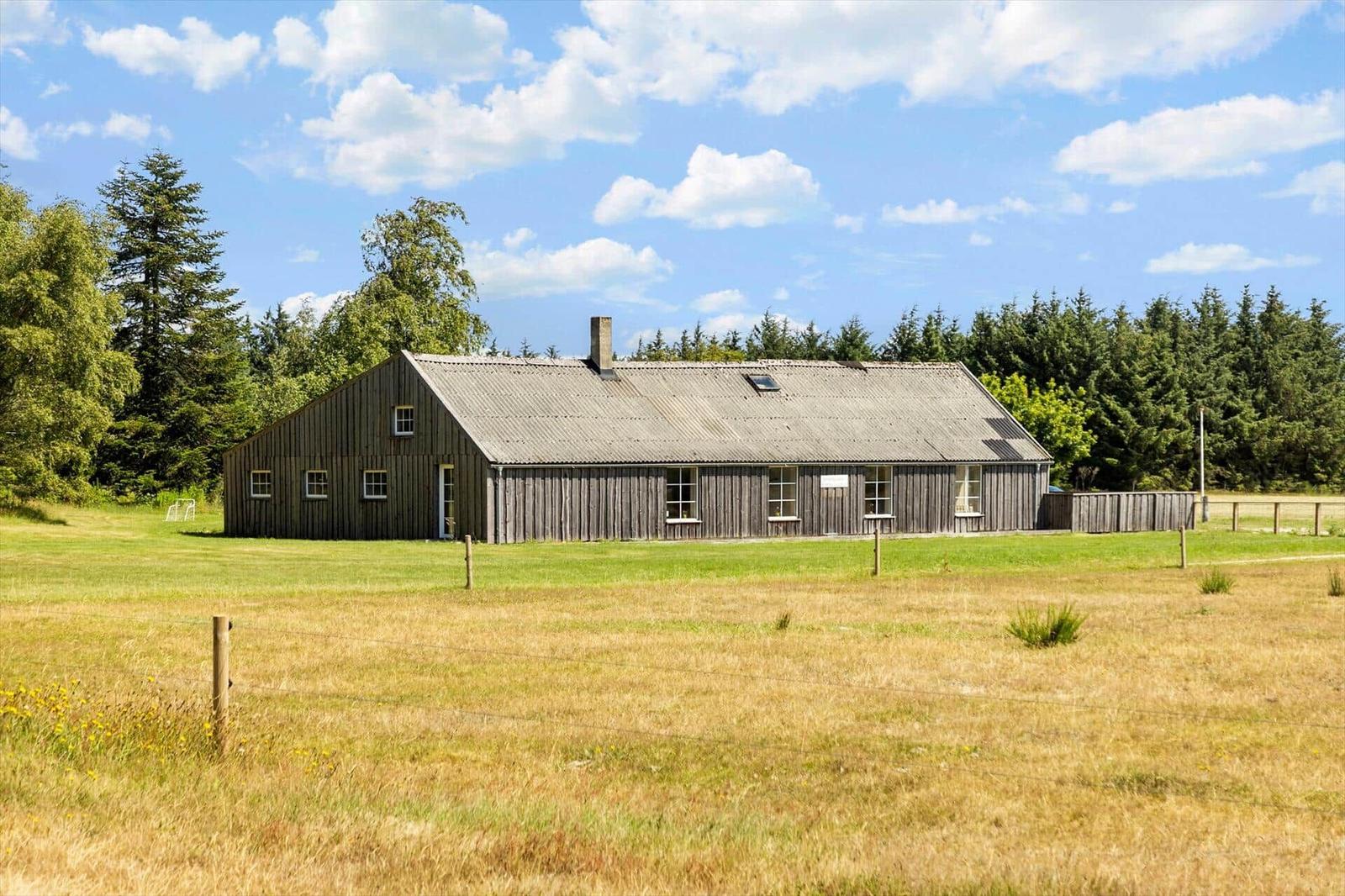 Holzhaus mit Schornstein und Dachfenster in ländlicher Umgebung mit Grasland und Bäumen.