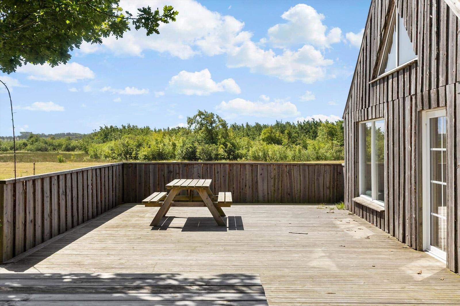 Holzterrasse mit Picknicktisch, Blick auf Wald und Himmel.