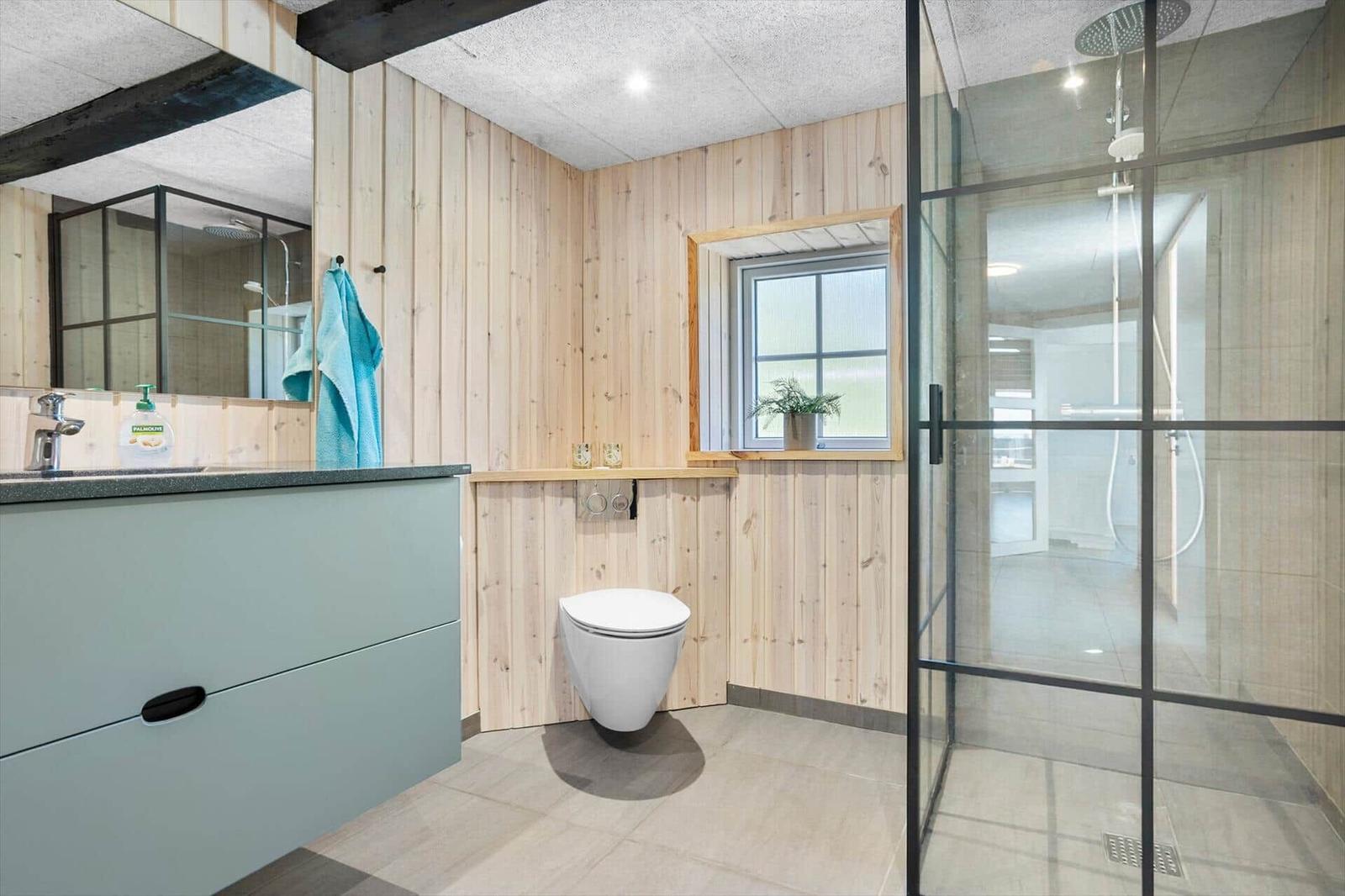 Badezimmer mit Dusche, Toilette und Waschbecken. Holzwände und Fenster.