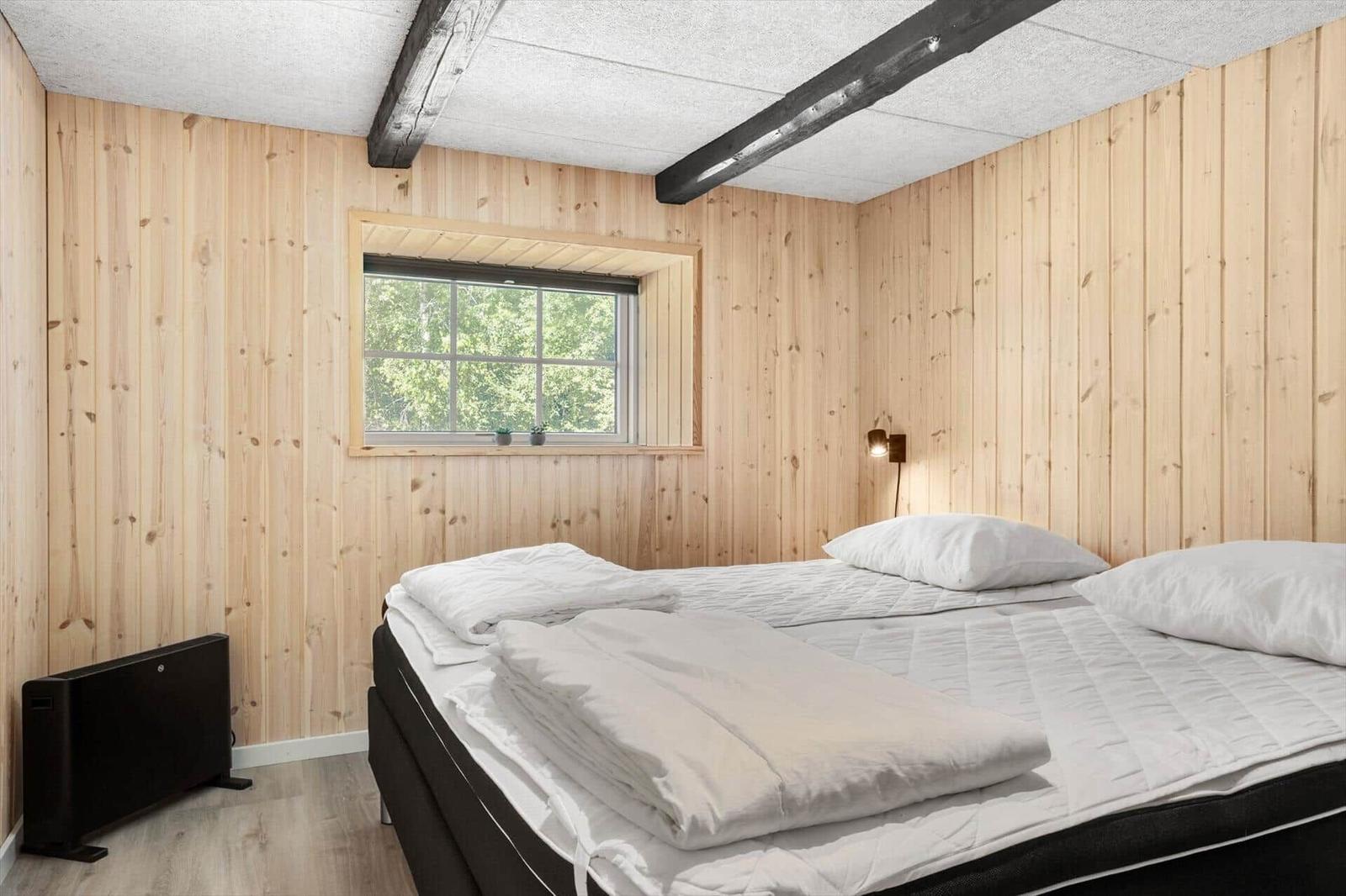 Schlafzimmer mit Holzwänden, Bett und Fenster mit Blick auf Bäume.