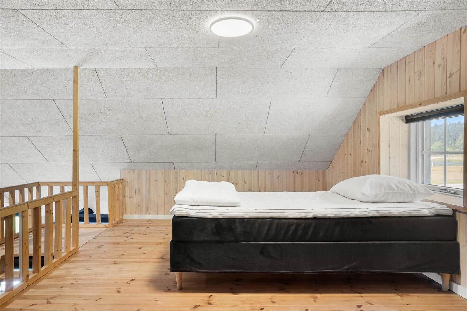 Schlafzimmer mit Bett, Holzfußboden und Fenster. Decke aus Holz und Kacheln.