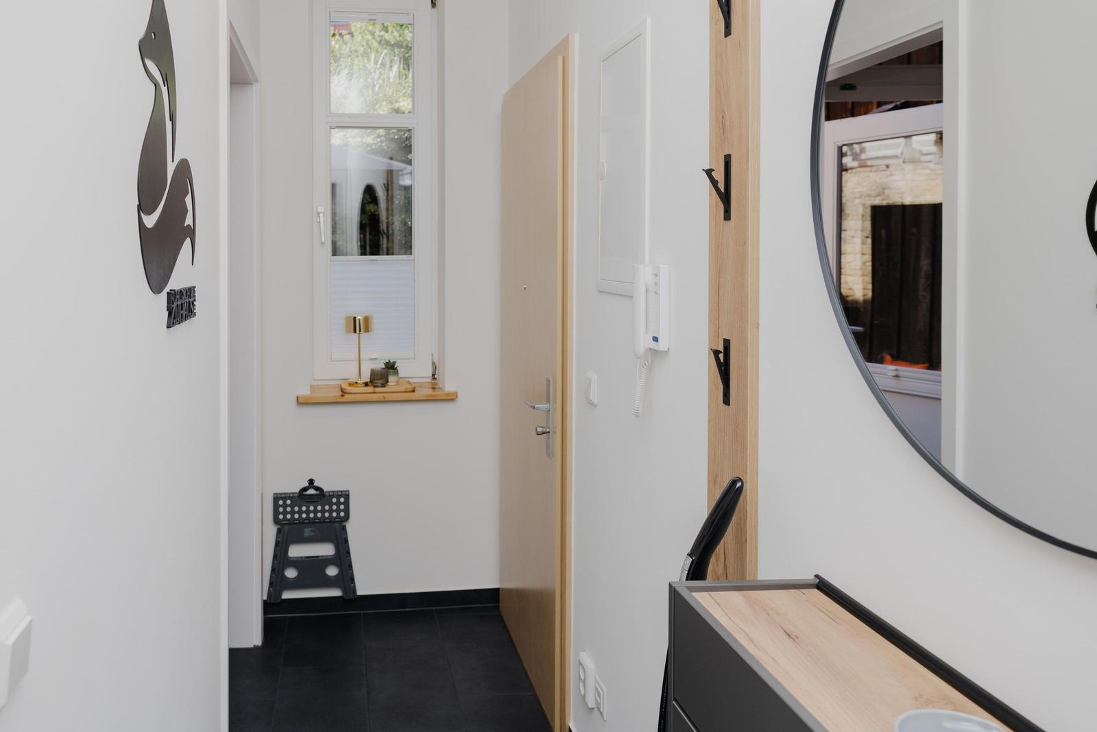 Eingangsbereich mit Wandspiegel, Tür und Fenster mit Holzbank.