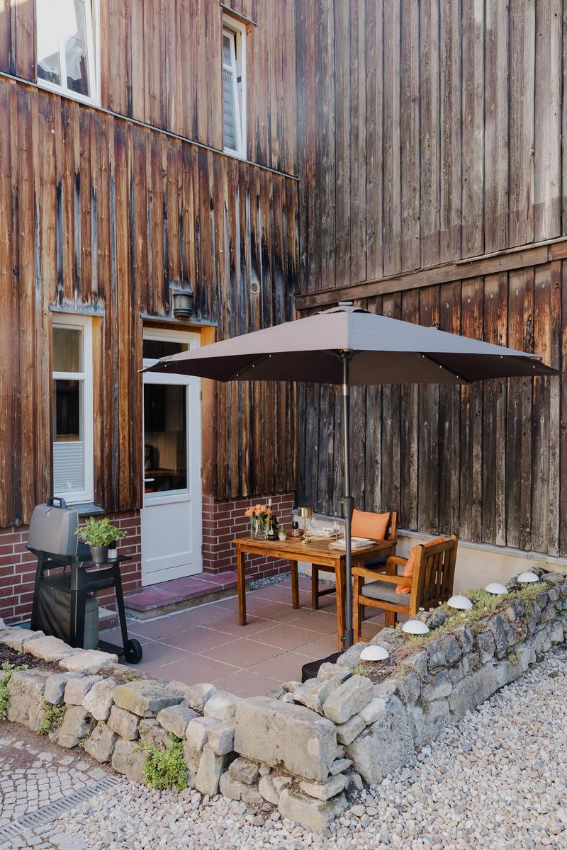 Terrasse mit Tisch, Stühlen und Sonnenschirm vor Holzhauswand