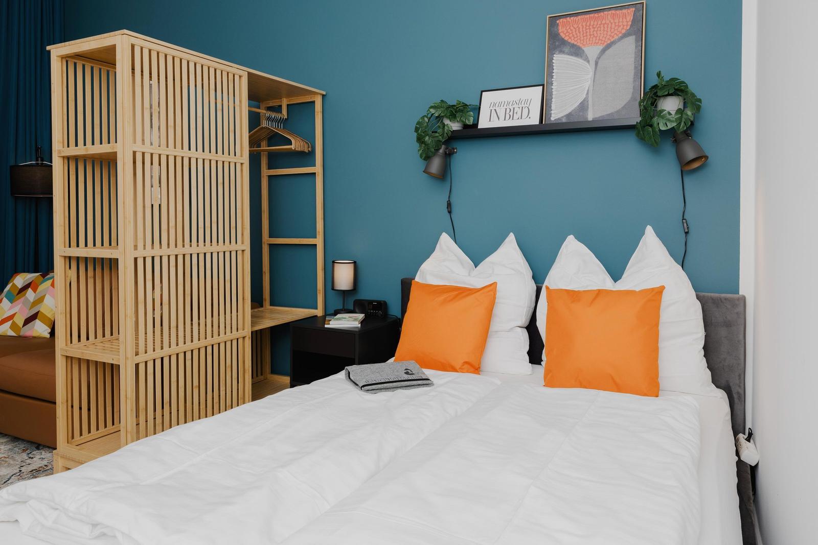 Schlafzimmer mit Bett, Kleiderschrank und Wandregal mit Pflanzen.