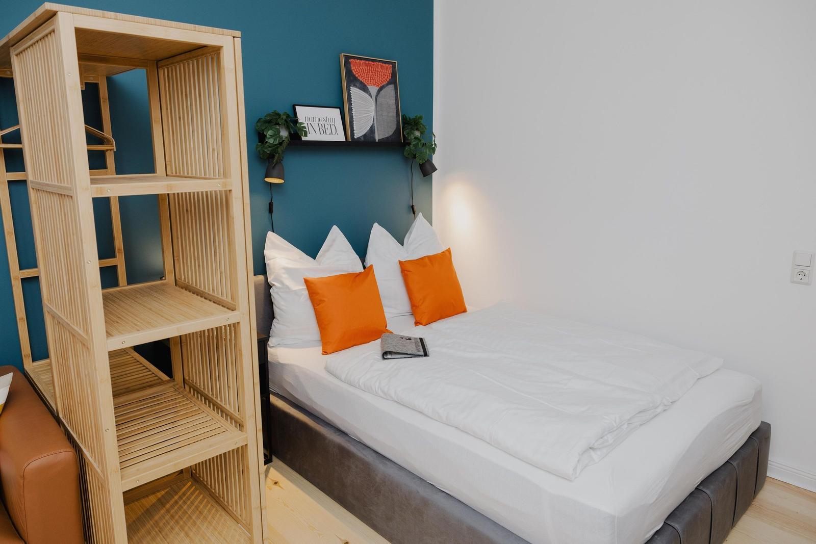 Schlafzimmer mit Bett, orangefarbenen Kissen und Holzregal an der Wand.