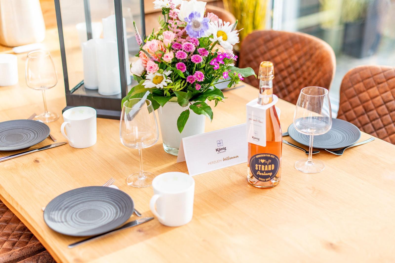 Tisch mit Blumen, Gläsern, Tassen und einer Flasche Rosé.