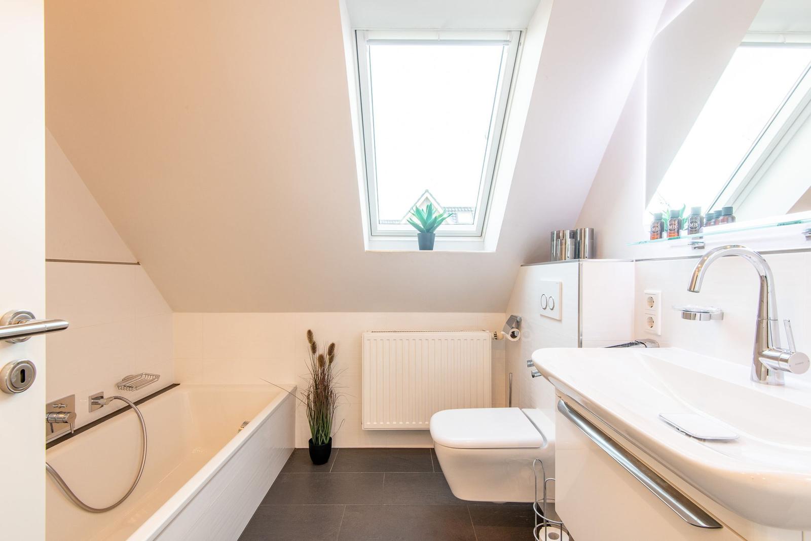 Badezimmer mit Dusche, Waschbecken und Toilette unter Dachschrägen mit Dachfenster.