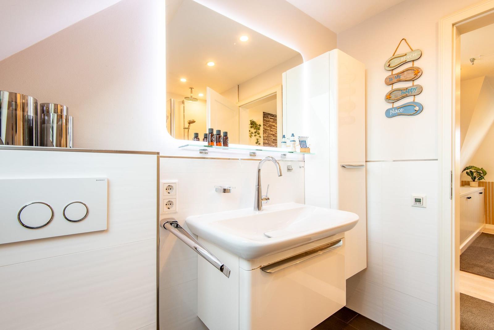 Badezimmer mit Waschbecken, Spiegel und Dusche. Wanddekoration mit Strandmotiv.