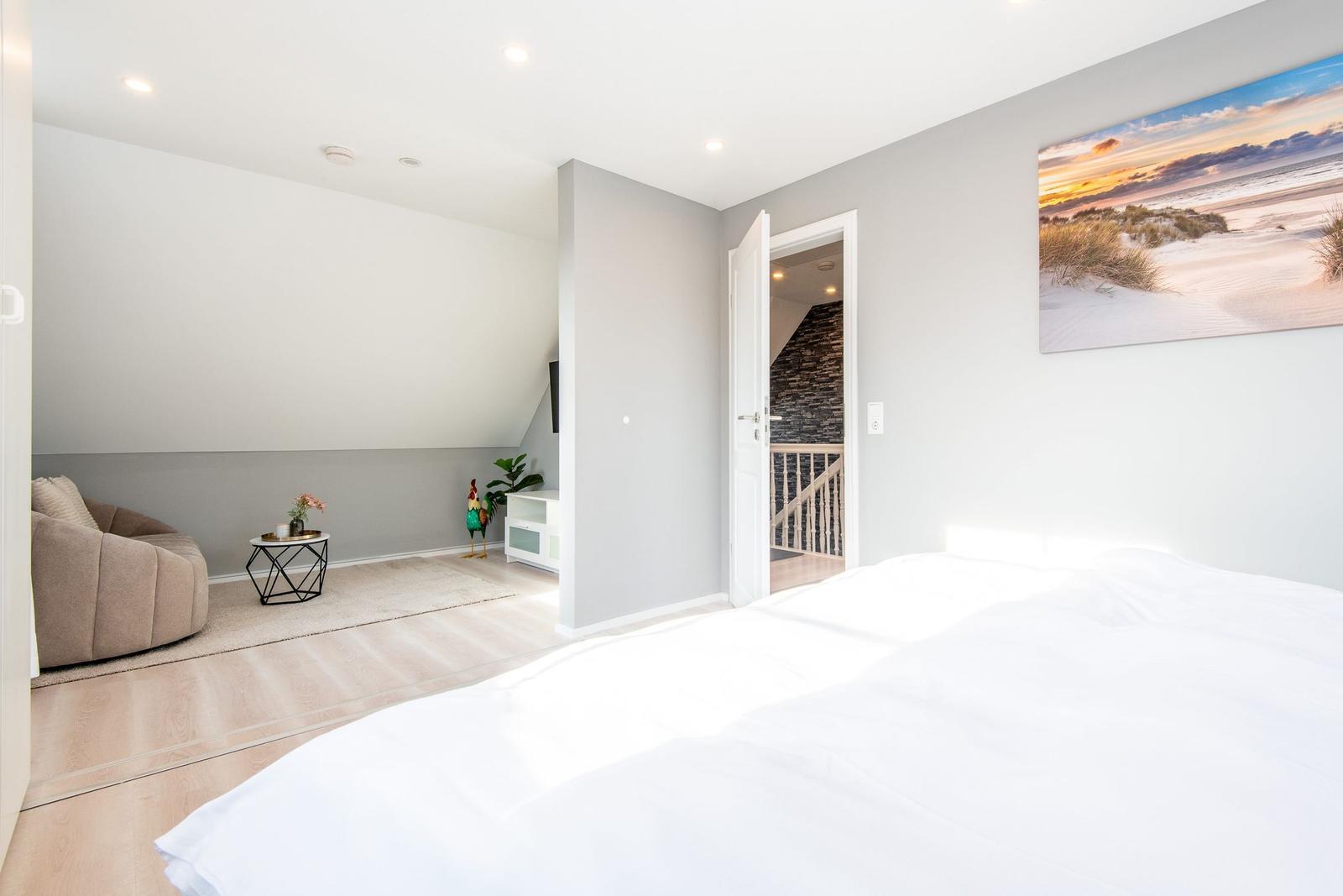Schlafzimmer mit weißem Bett, Wandbild und Tür zum Treppenhaus.