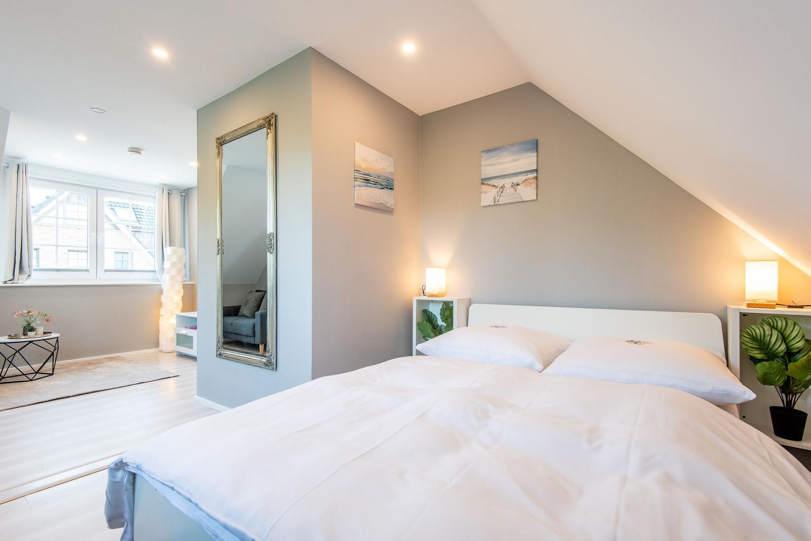Schlafzimmer mit Doppelbett, Spiegel und Fenster. Wandbilder und Nachttische mit Lampen.