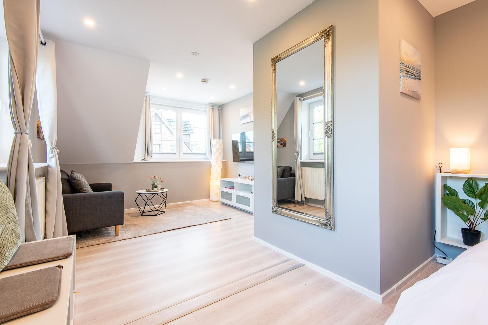 Wohnbereich mit Sofa, Spiegel und Fenster. Holzboden und Wandgestaltung.