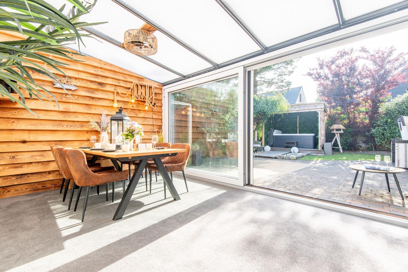 Terrasse mit Essbereich und Blick auf den Garten. Holzwand und Glasfront.