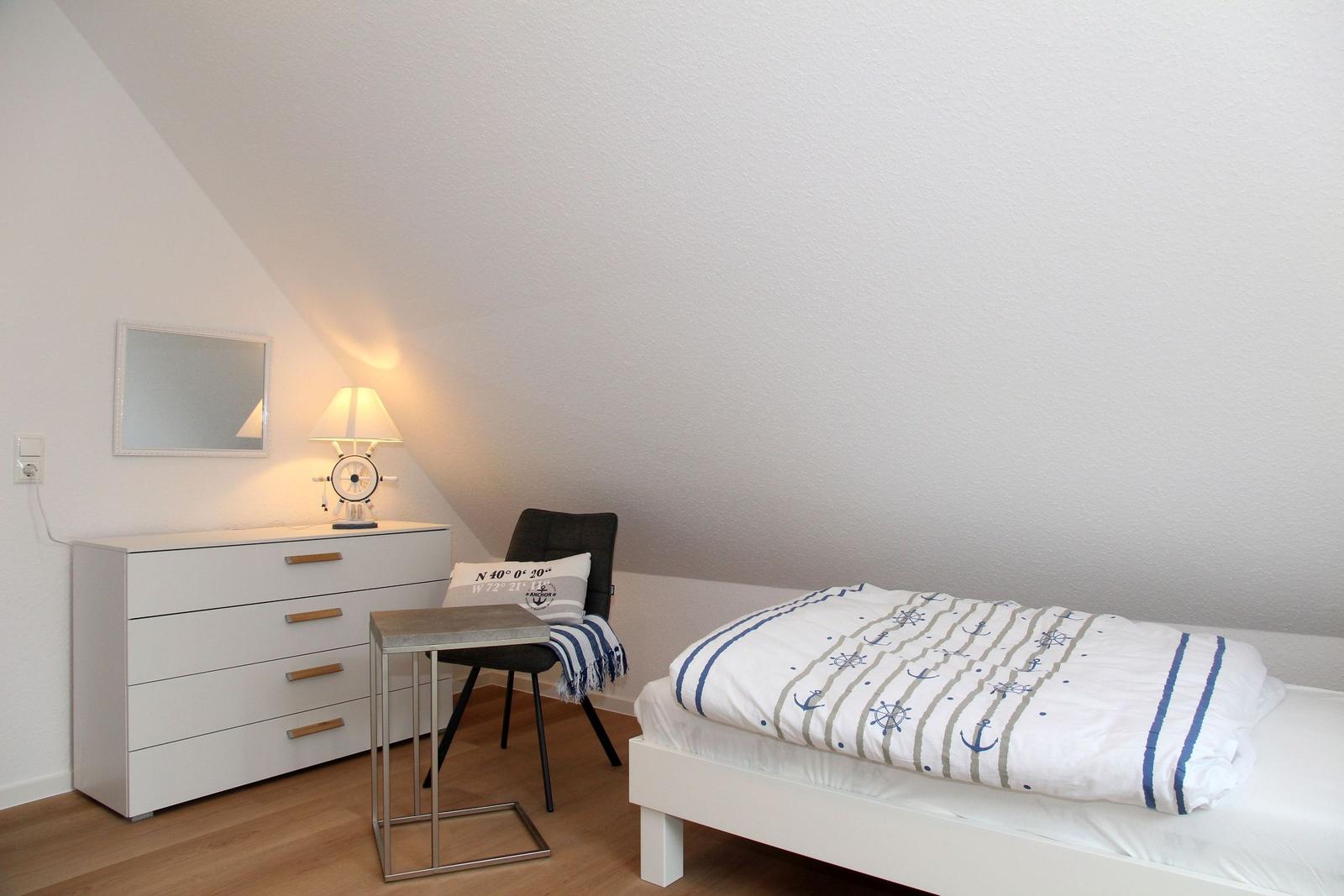 Schlafzimmer mit Bett, Kleiderschrank und Stuhl unter schräger Decke.