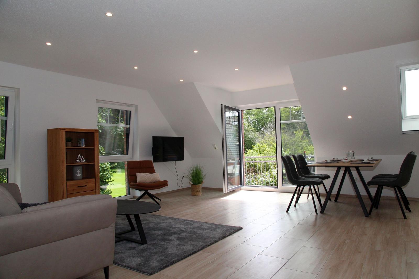 Wohn- und Essbereich mit Balkon, TV, Sofa und Tisch.