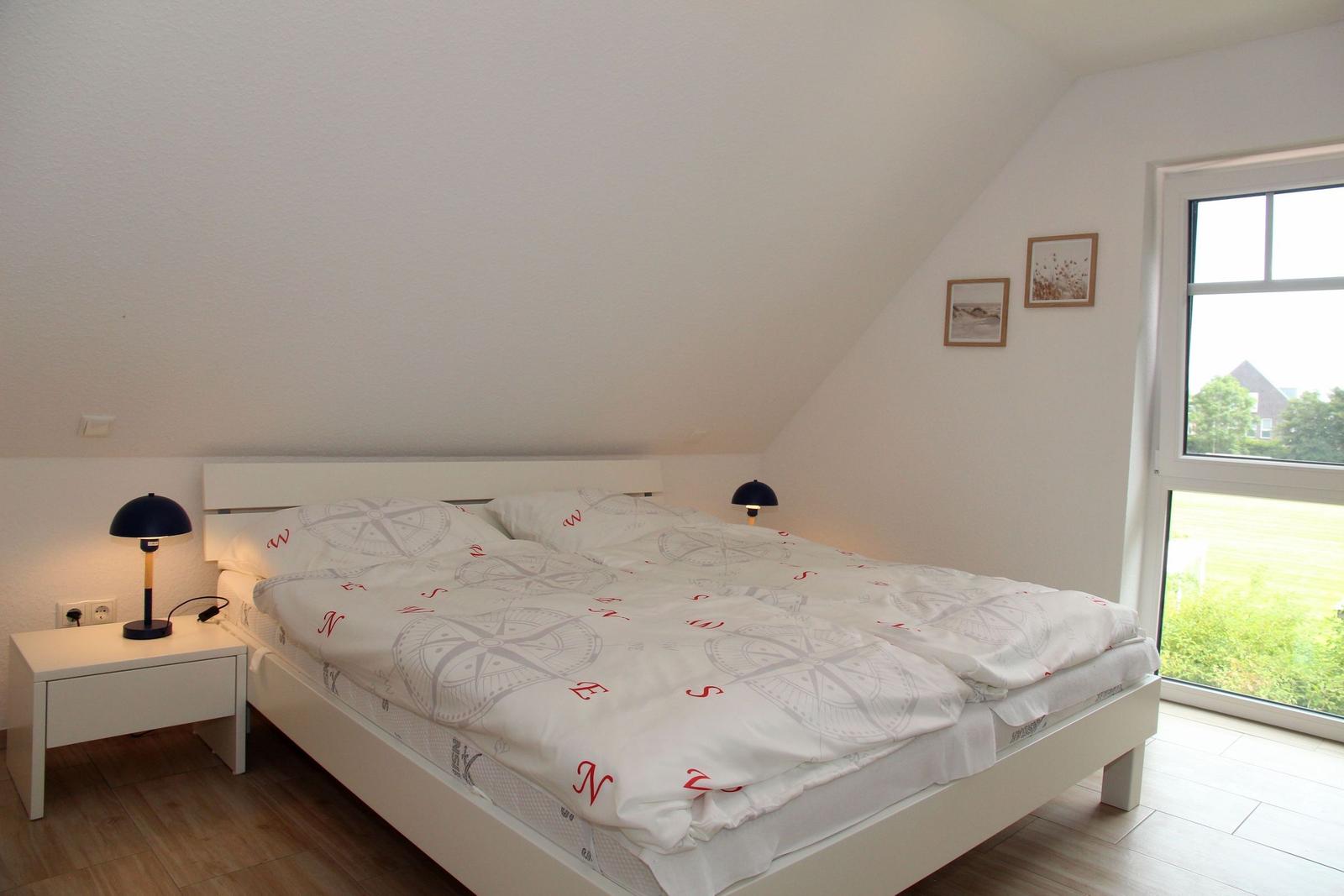 Schlafzimmer mit Doppelbett, zwei Nachttischen und großem Fenster mit Blick auf Grünflächen.