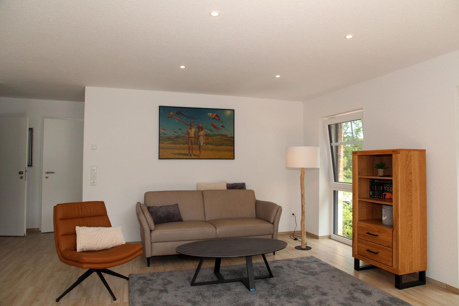 Wohnzimmer mit Sofa, Sessel, Tisch und Regal. Wandbild und Fenster mit Blick nach draußen.