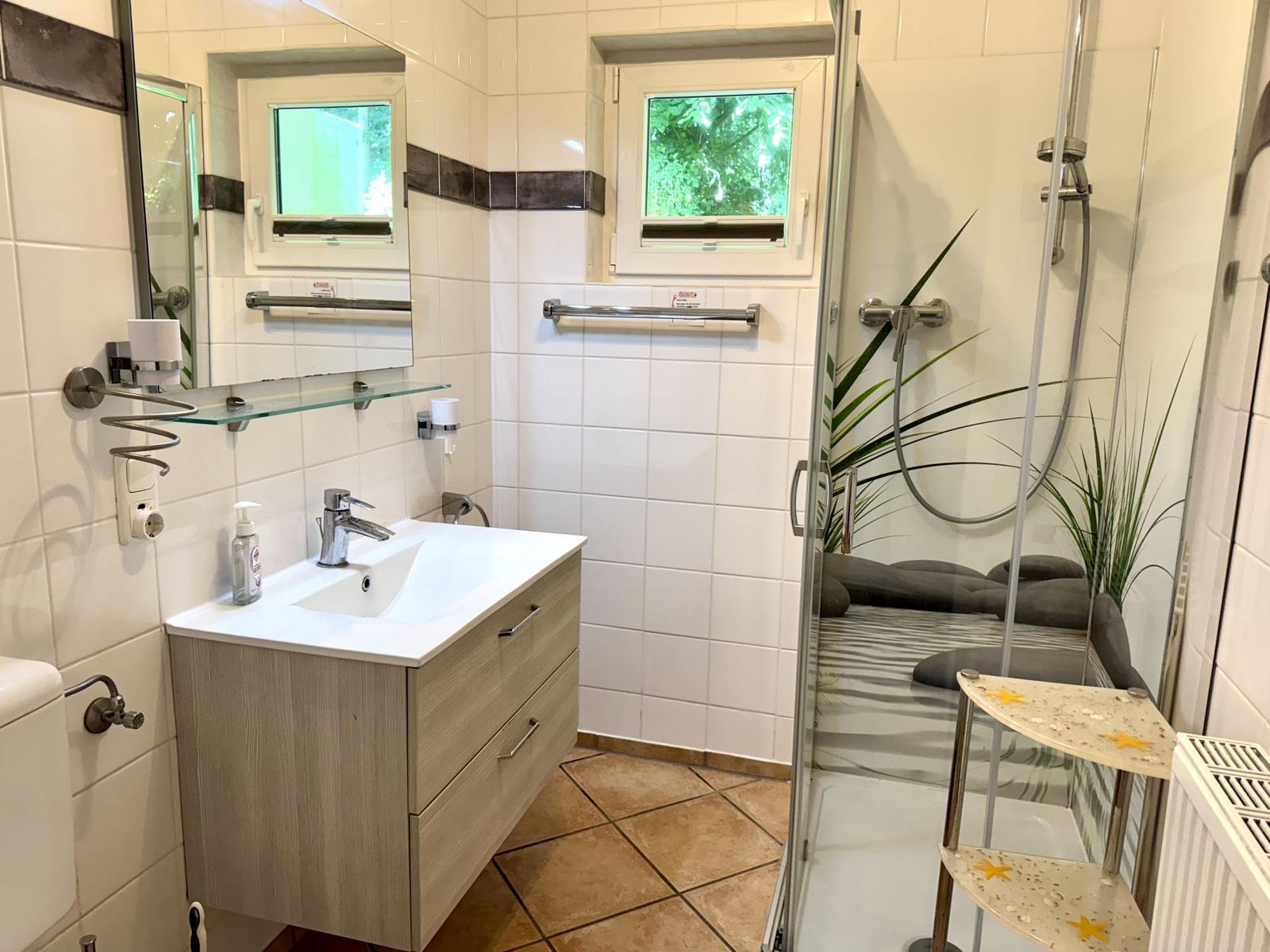 Badezimmer mit Dusche, Waschbecken und Fenster.