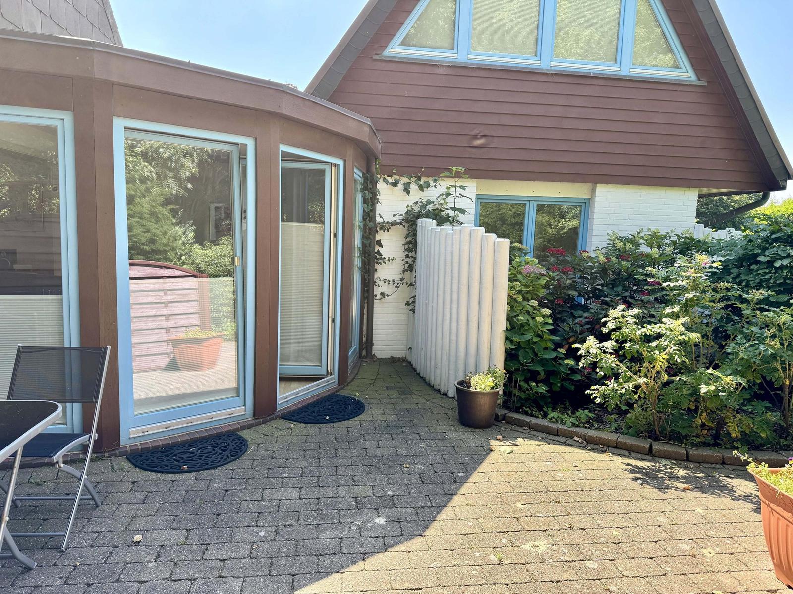 Terrasse mit Sitzgelegenheit, Garten und Haus mit Fenstern.
