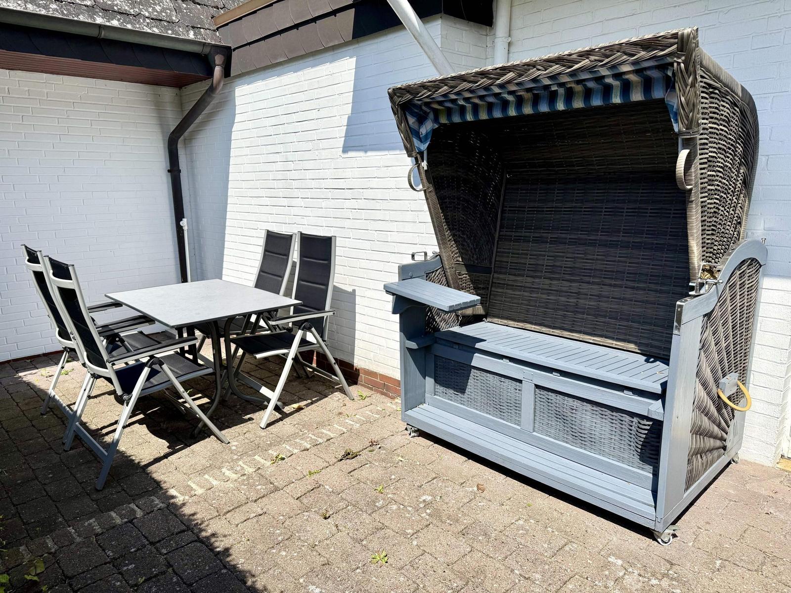 Terrasse mit Tisch, Stühlen und Liegestuhl mit Schutzdach.