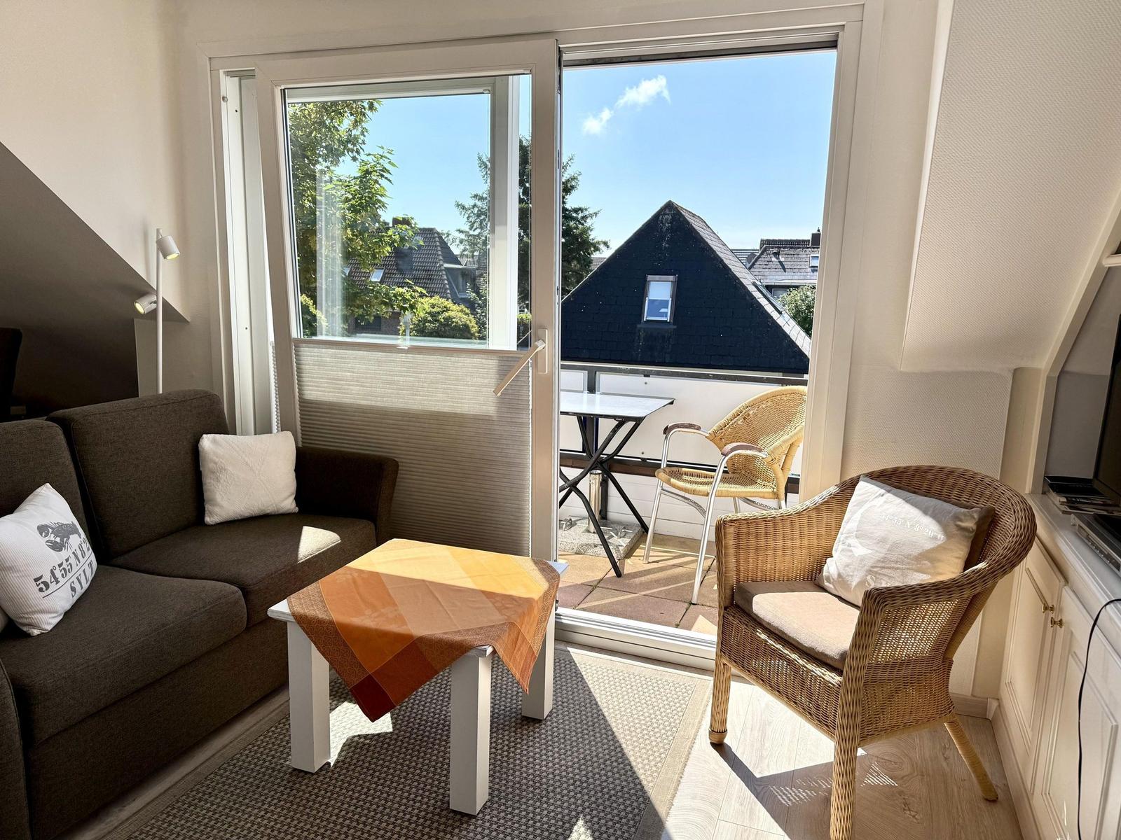 Living room with sofa, armchair, and balcony with table and chairs.