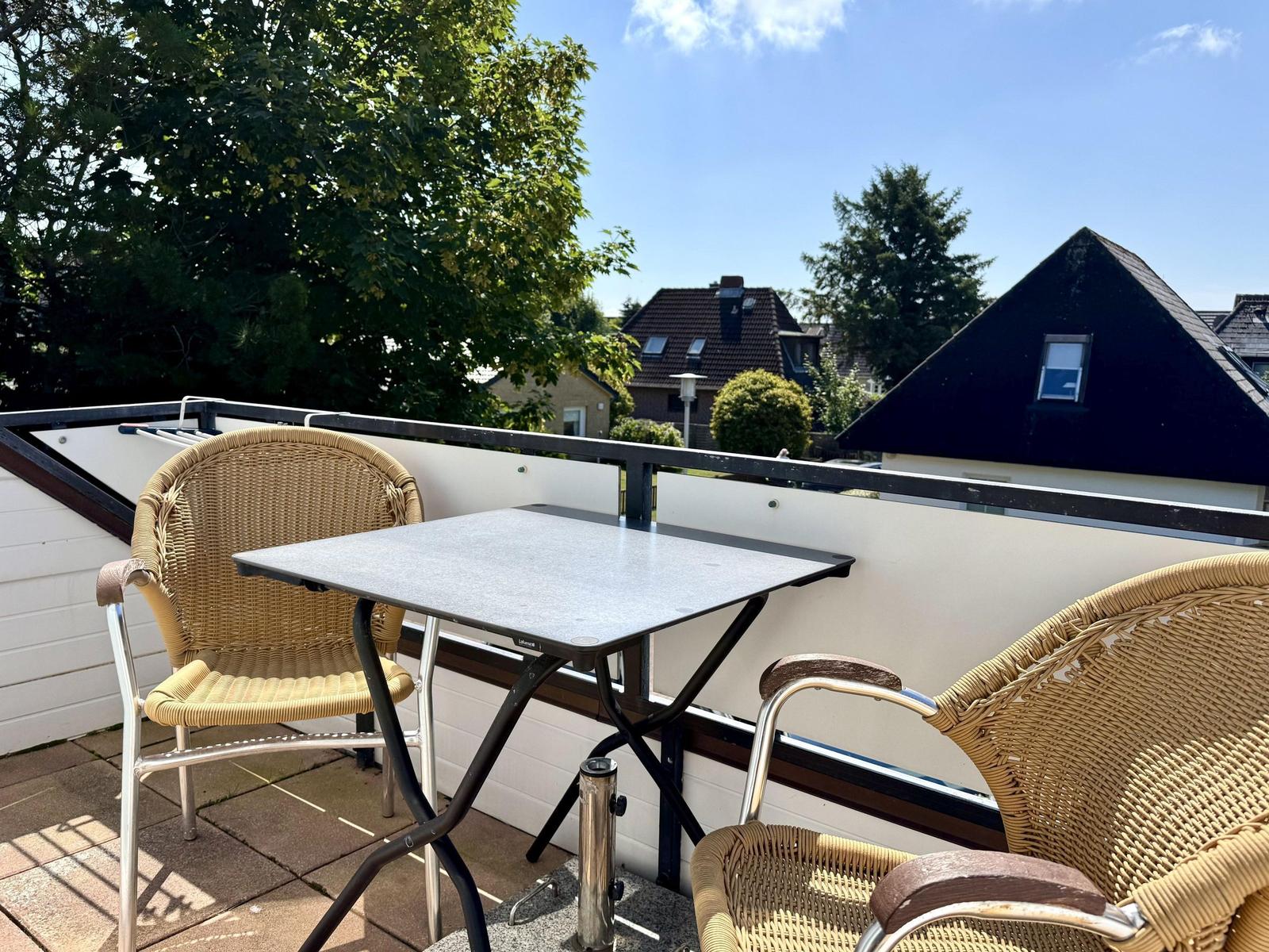 Terrace with table and two chairs. View of houses and trees.
