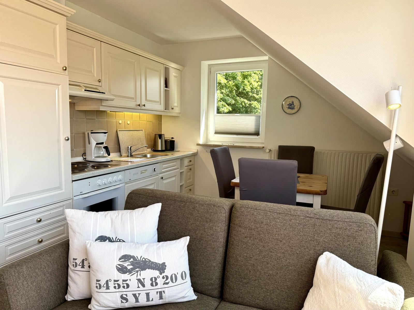 Living area with kitchen, dining table, and sofa under sloped ceilings.