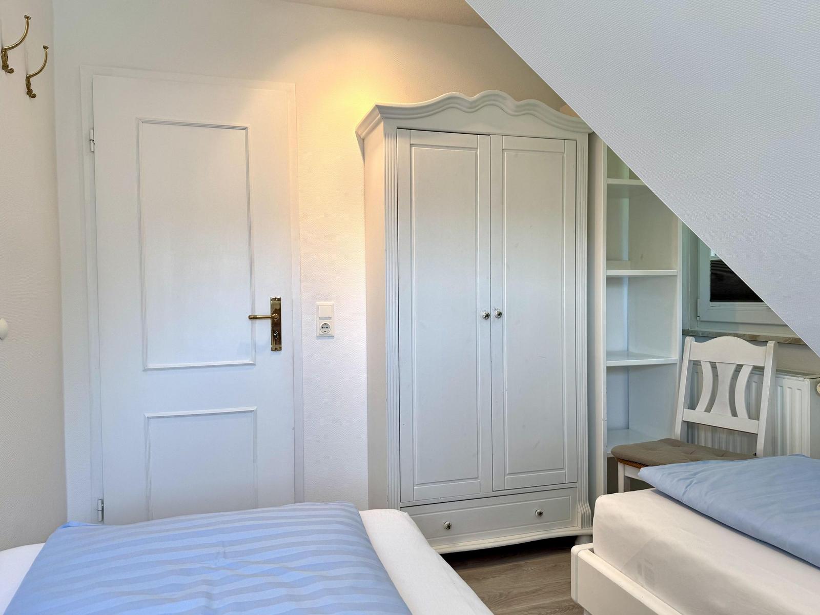 Room with two beds, wardrobe, and chair under sloped ceiling.