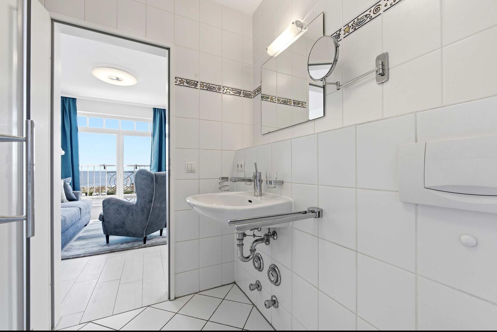 Badezimmer mit Waschbecken und Spiegel. Durchgang in Wohnzimmer mit Blick auf Balkon.