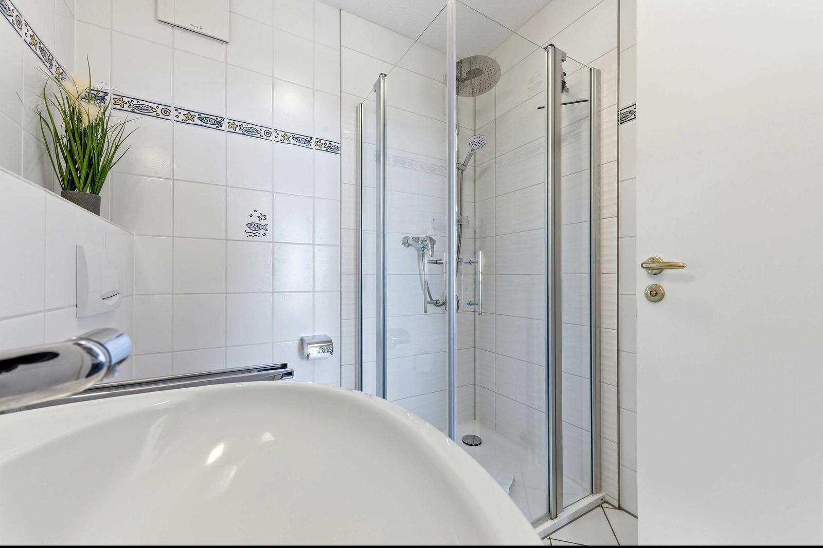 Badezimmer mit Dusche, Waschbecken und dekorativen Fliesen.