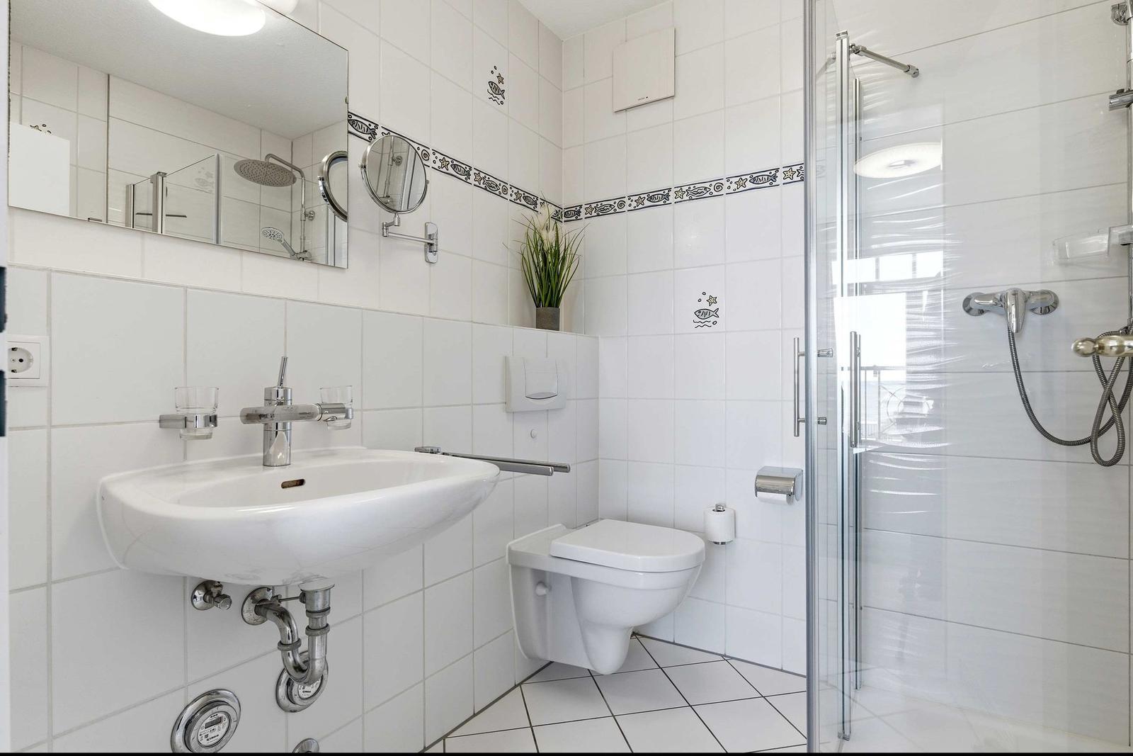 Badezimmer mit Dusche, Toilette und Waschbecken. Weiße Fliesen und Spiegel.